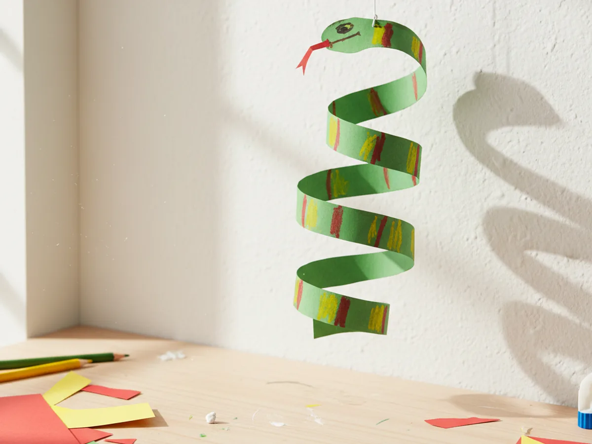 A paper spiral snake cut from a colorful sheet of paper with stripes hanging from a string