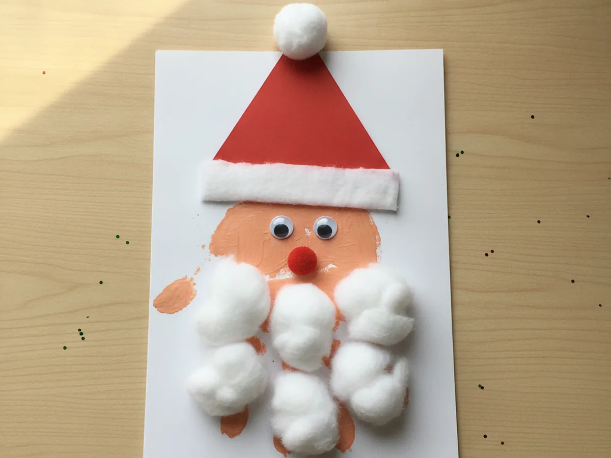 Handprint Santa Claus with a peach painted palm face, cotton ball beard on the fingers, and a red paper hat