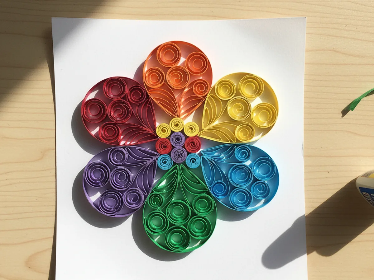 Colorful paper quilling spirals arranged into a flower shape on white cardstock