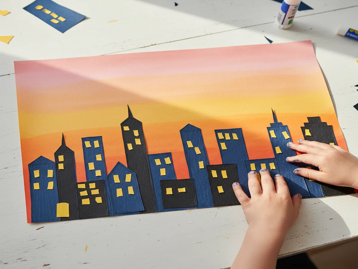 Handmade paper city skyline silhouette with buildings cut from dark paper on a colorful sunset background