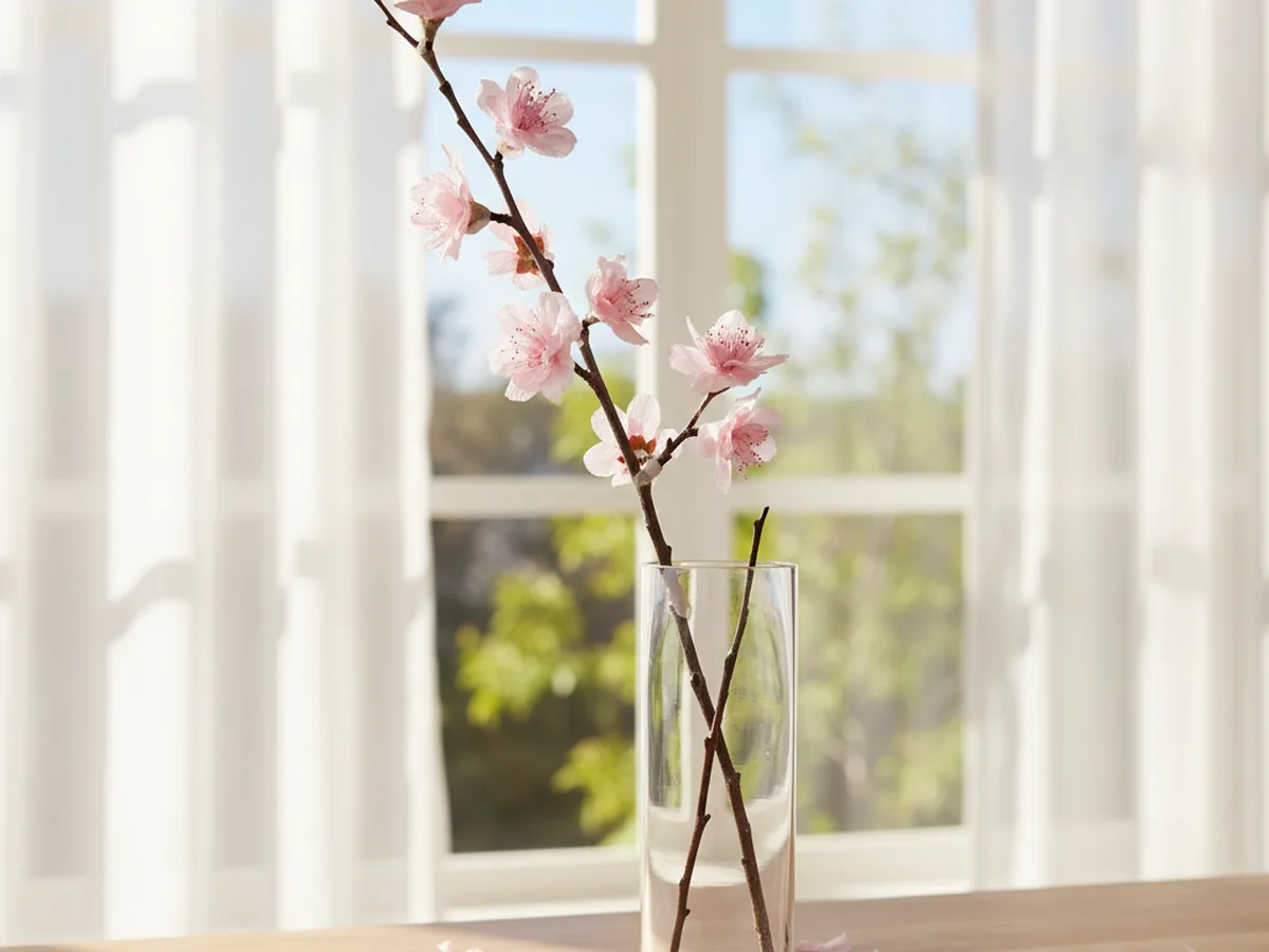 Handmade cherry blossom branch with pink crepe paper flowers attached to a real twig in a tall vase