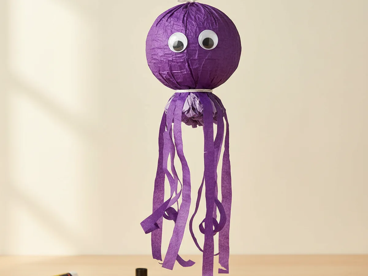 Handmade purple crepe paper octopus with a round head, eight wavy streamer legs, and two googly eyes