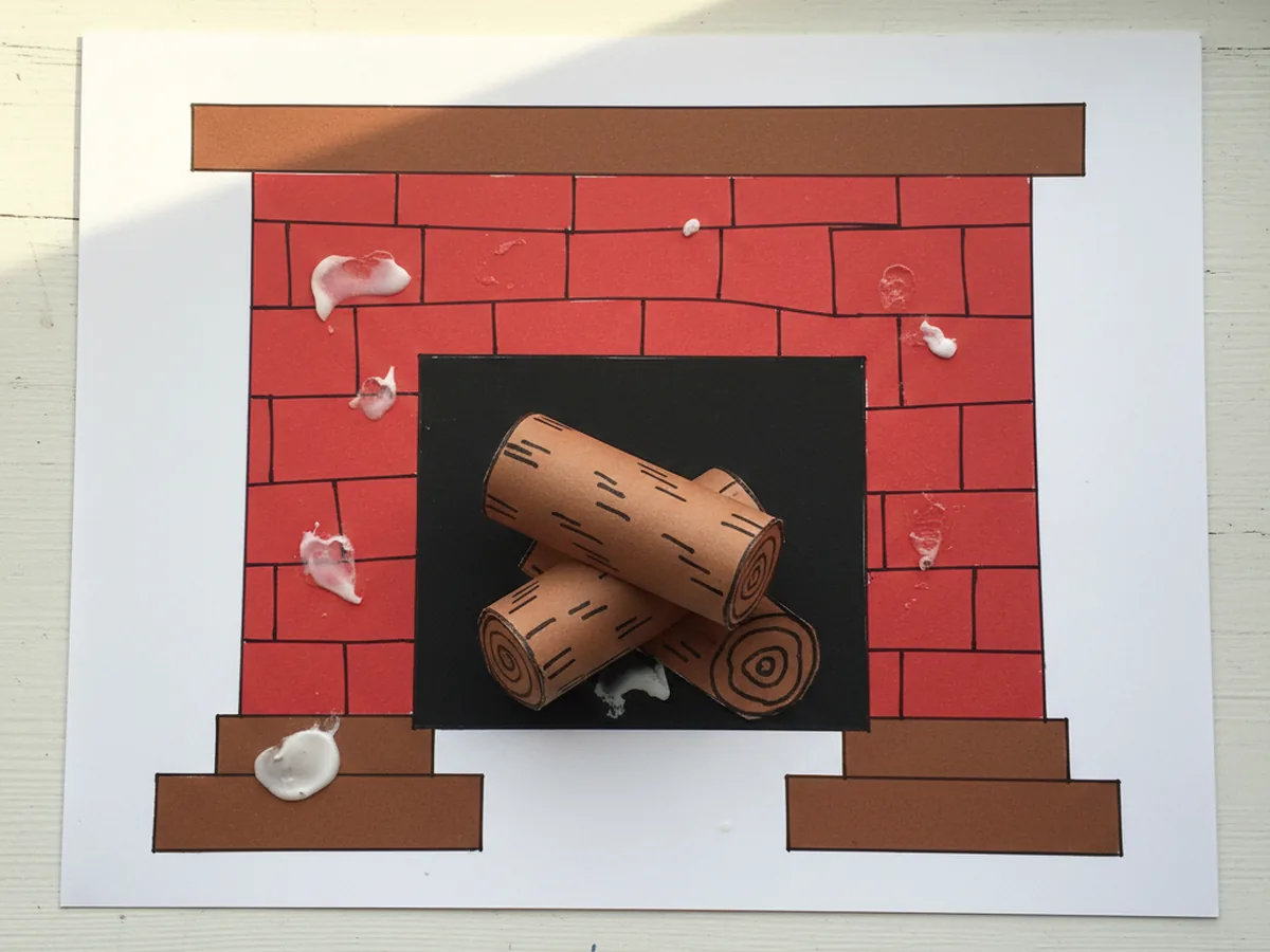 Two brown paper logs with marker bark details glued at the bottom of the black firebox opening of the paper fireplace