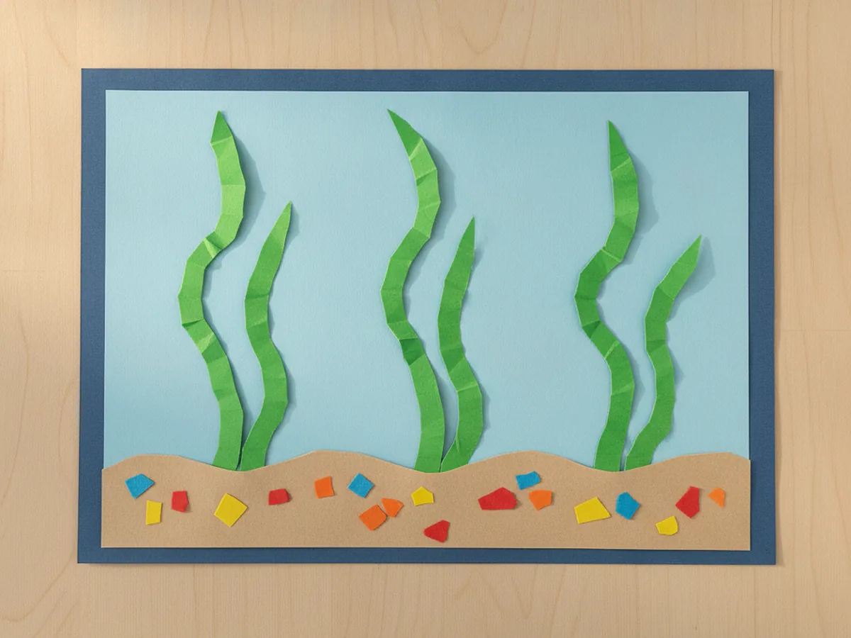 Tall wavy green paper seaweed strips glued standing up from the sand inside the blue paper fish tank