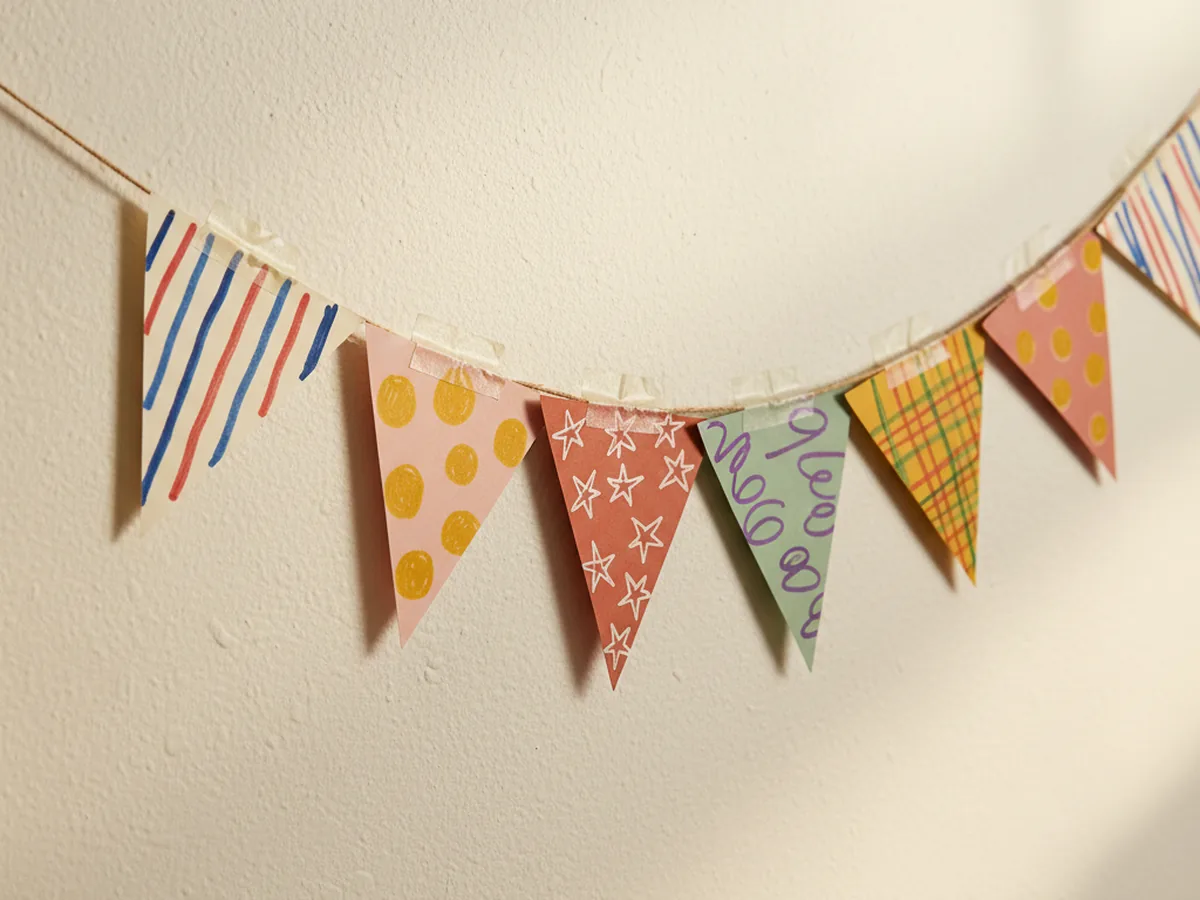A handmade geometric paper triangle bunting with colorful pennants decorated with stripes and dots strung on twine and hung along a wall