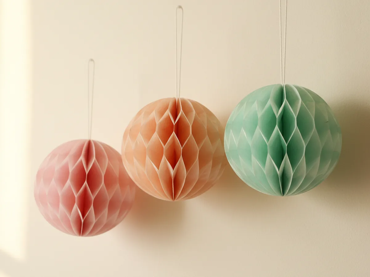 A handmade honeycomb paper wall display with three 3D tissue paper honeycomb balls in pink, peach, and mint hanging at different heights on a light wall