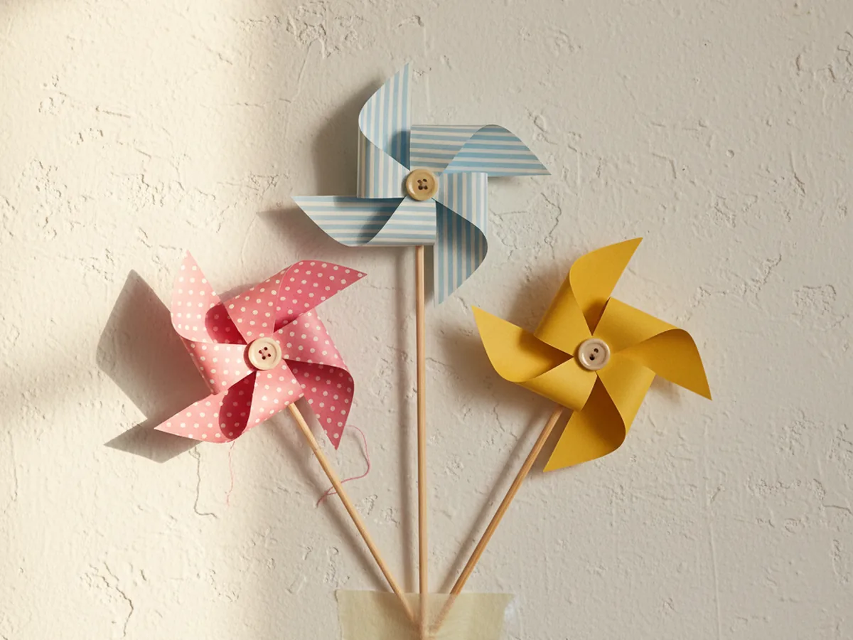 A handmade paper pinwheel wall cluster with three colorful paper pinwheels in pink, blue, and yellow mounted together on a light wall