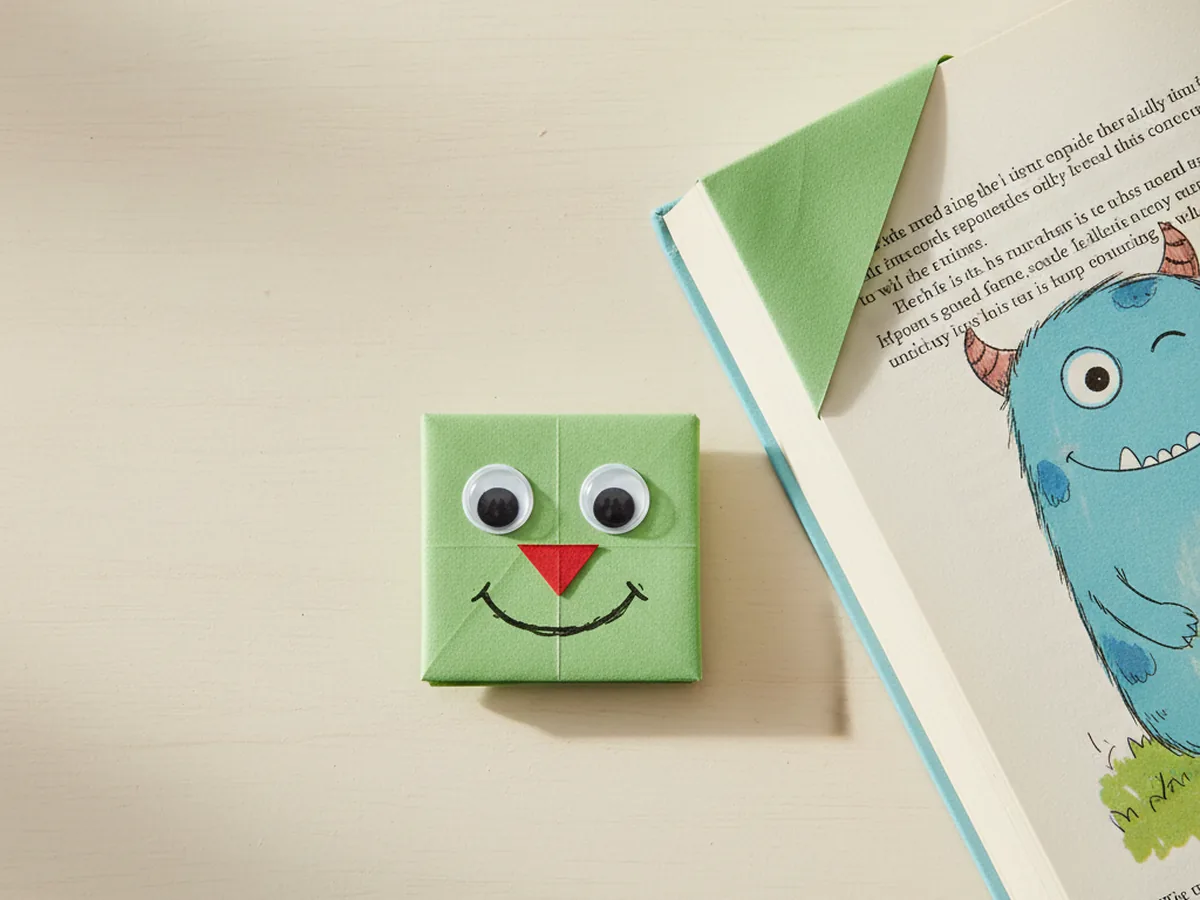A handmade origami corner bookmark decorated as a smiling face on the corner of an open book