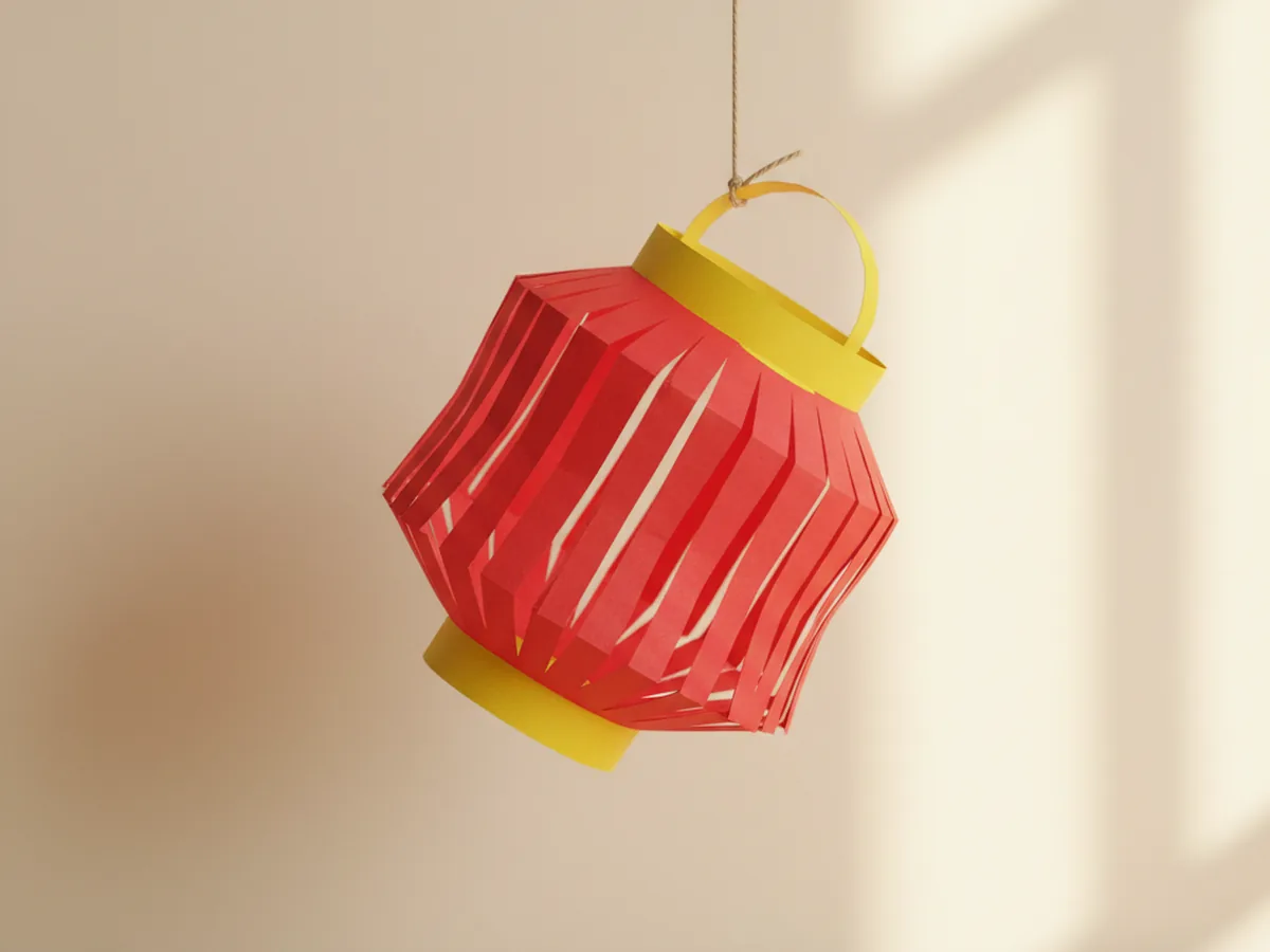 A handmade red and yellow paper lantern in the chochin style hanging from a thread on a light wall