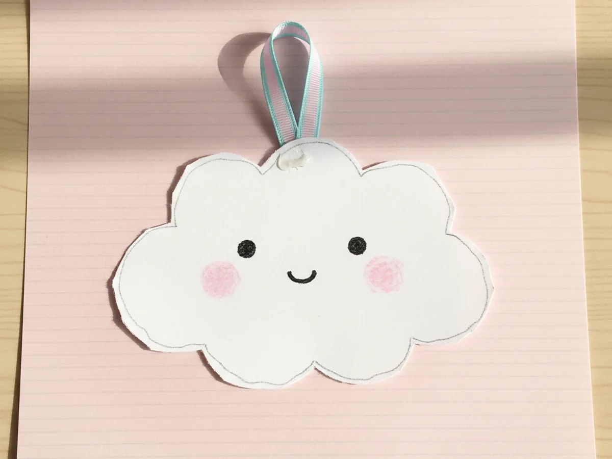 Handmade white paper kawaii cloud with tiny dot eyes, a small curved smile, and pink blush cheeks