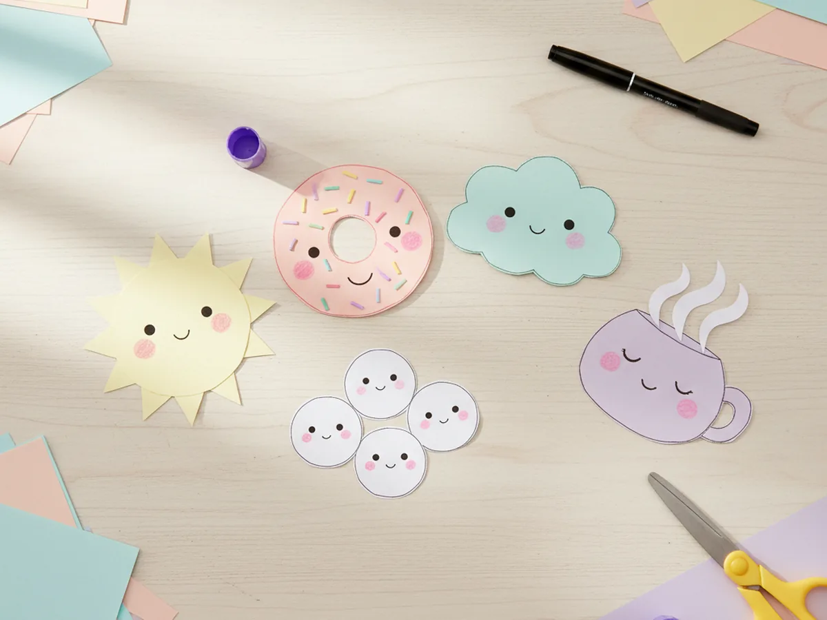 A pastel spread of handmade kawaii paper crafts with smiling faces including clouds, sushi, donuts, and tea cups on a craft table
