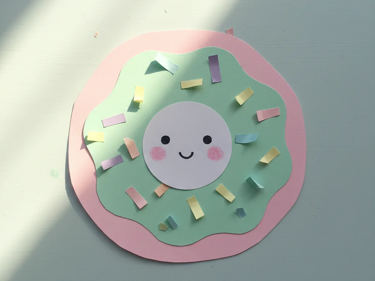 Handmade kawaii pastel pink paper donut with sprinkles and a tiny smiling face on the icing