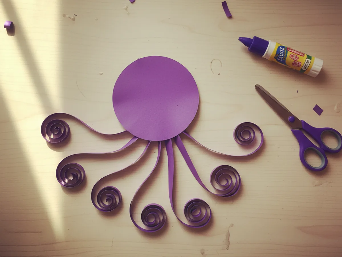 A round purple octopus head with eight curled purple paper tentacles glued to the bottom edge, fanning out evenly to form the body of the octopus on a light wood craft table