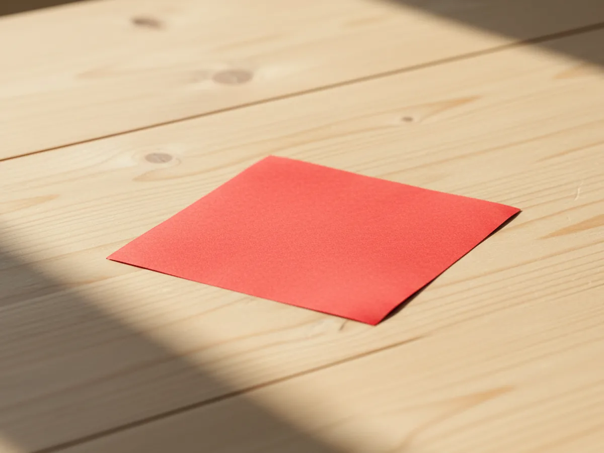 A single colorful square of origami paper placed flat on a light wood craft table, ready to fold