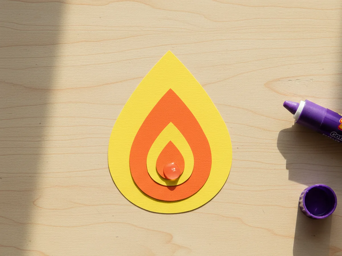 The orange teardrop flame glued and centered on top of the larger yellow teardrop flame, showing a two-tone candle flame with yellow outer halo and orange center on a craft table