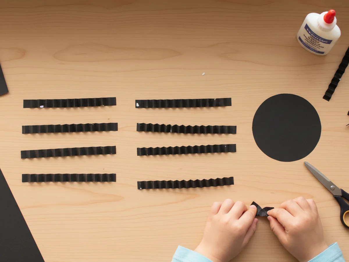 Eight black paper strips folded into accordion zigzag legs ready to be glued onto a paper spider body