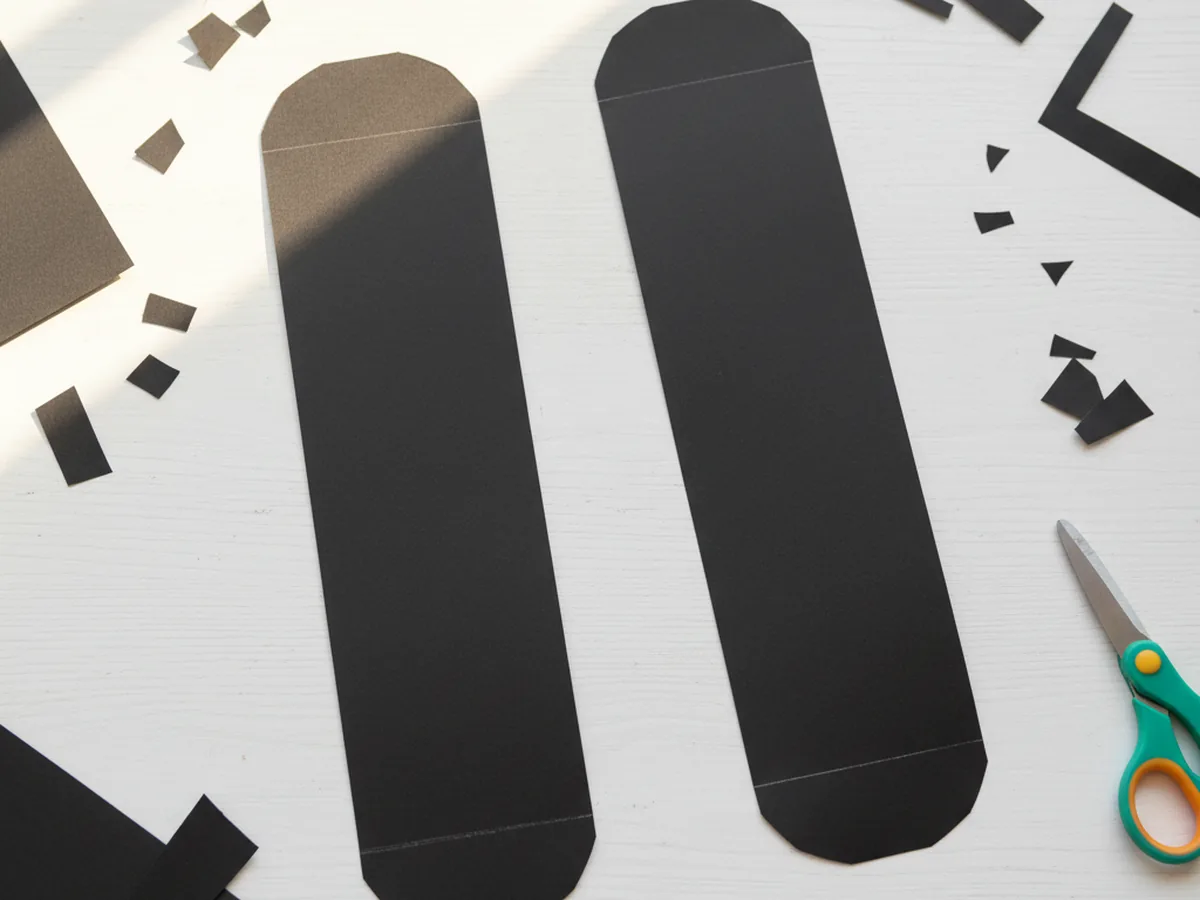 Two long black paper tread shapes with rounded ends cut from construction paper for a paper craft tank