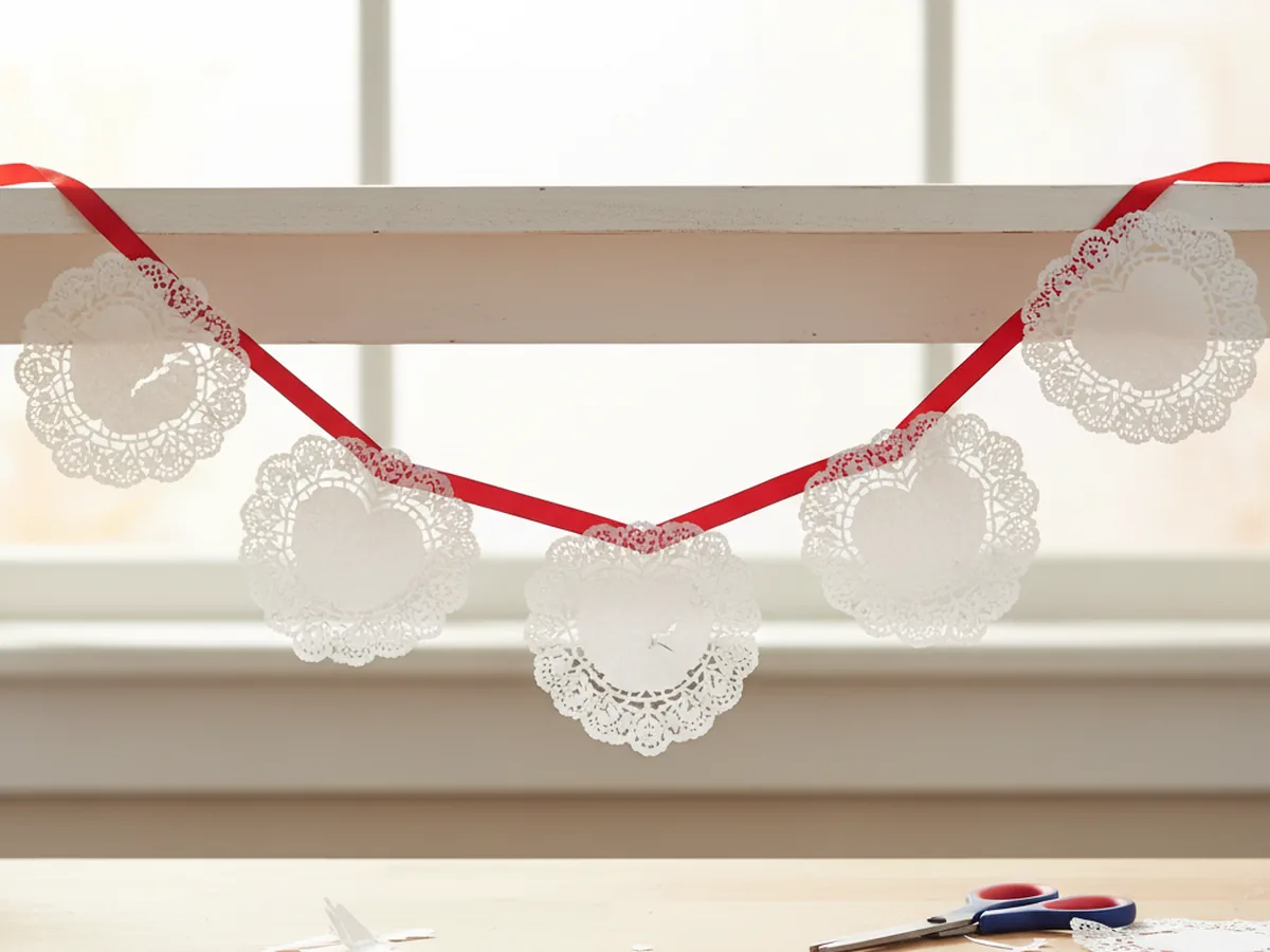Paper doily heart garland with red ribbon hung along a shelf for Valentine's Day