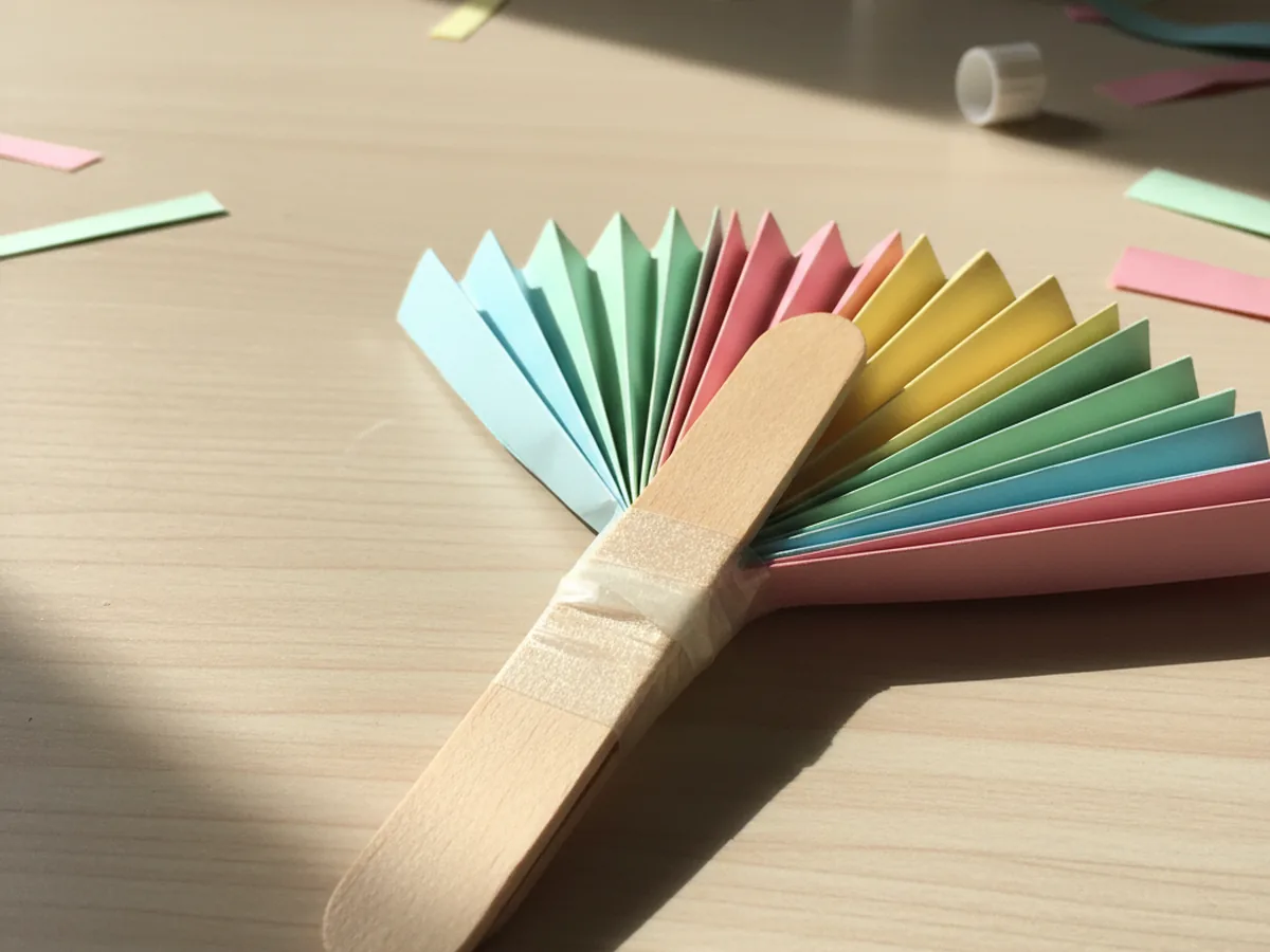 Clear tape wrapped tightly around the pinched base of a paper fan craft to hold the accordion folds together