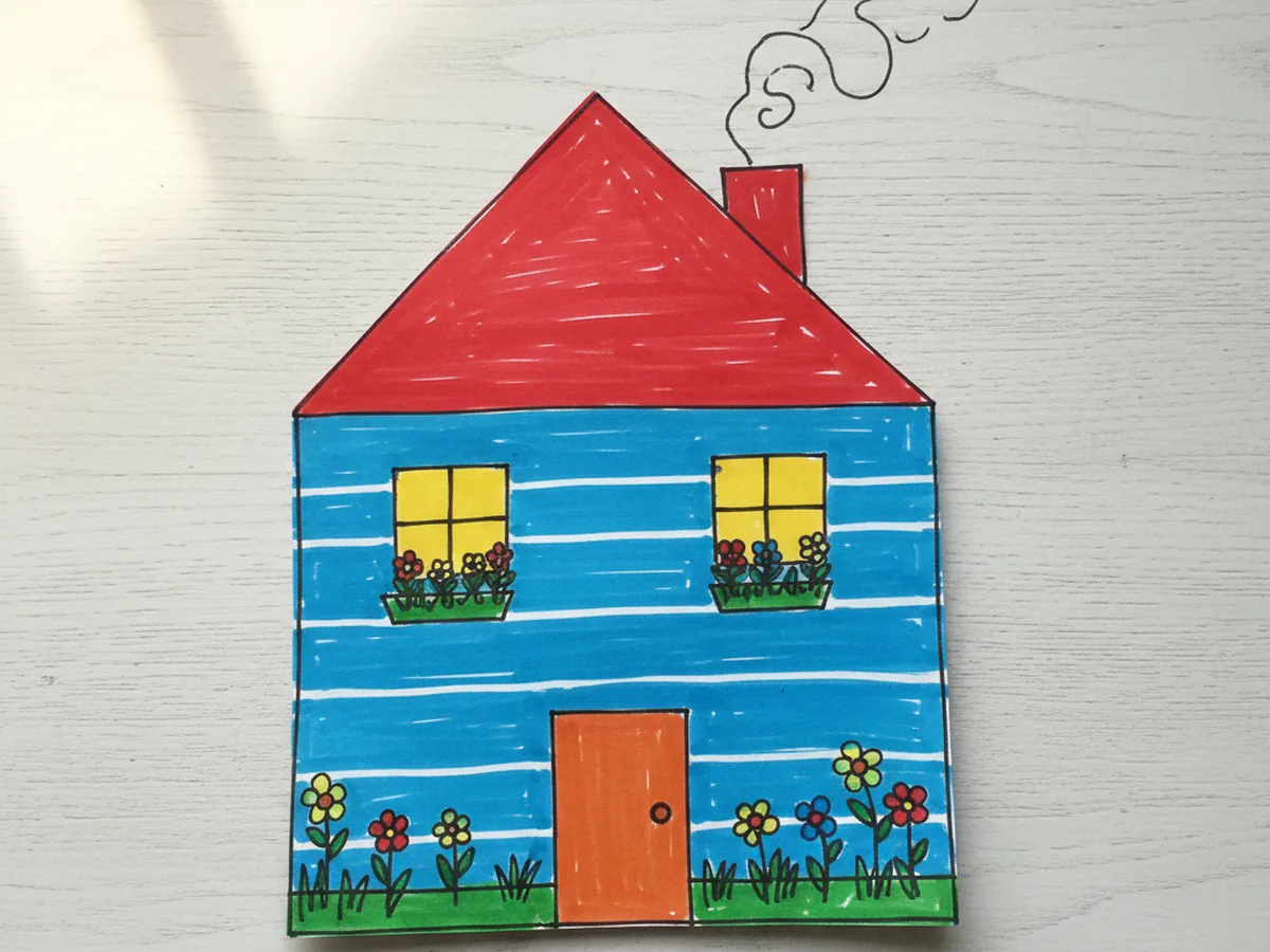 Finished colorful paper house craft made from construction paper with a red triangle roof, blue walls, and yellow windows on a white craft table