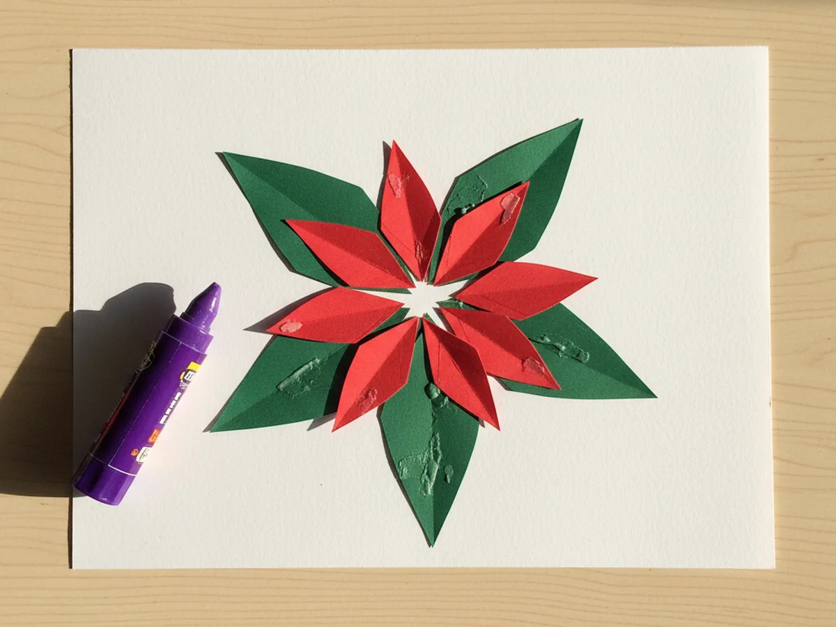 Six red pointed paper petals layered on top of the five green leaves and slightly rotated so the red points peek out between the green points, forming a bright red and green poinsettia bloom on white cardstock