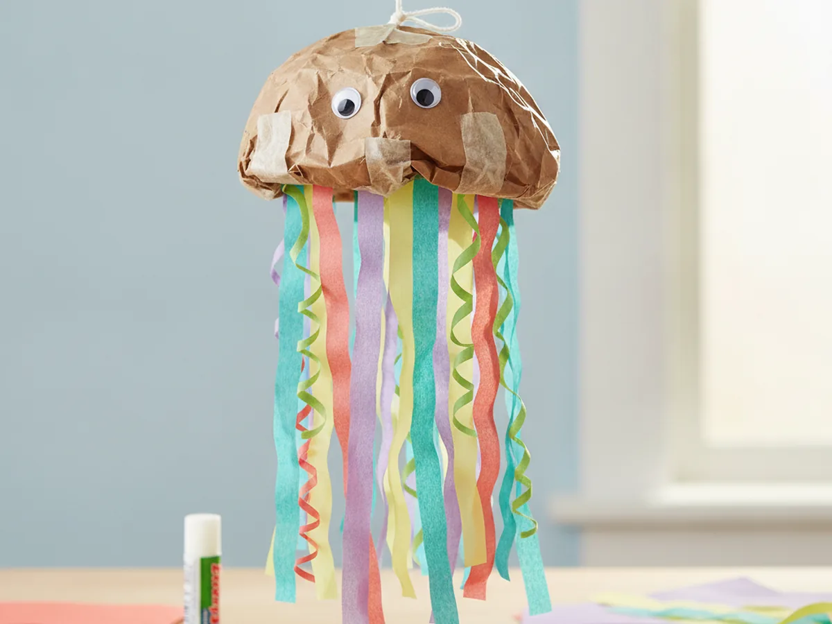 Handmade paper bag jellyfish with a rounded dome body and long tissue paper and streamer tentacles hanging from a string
