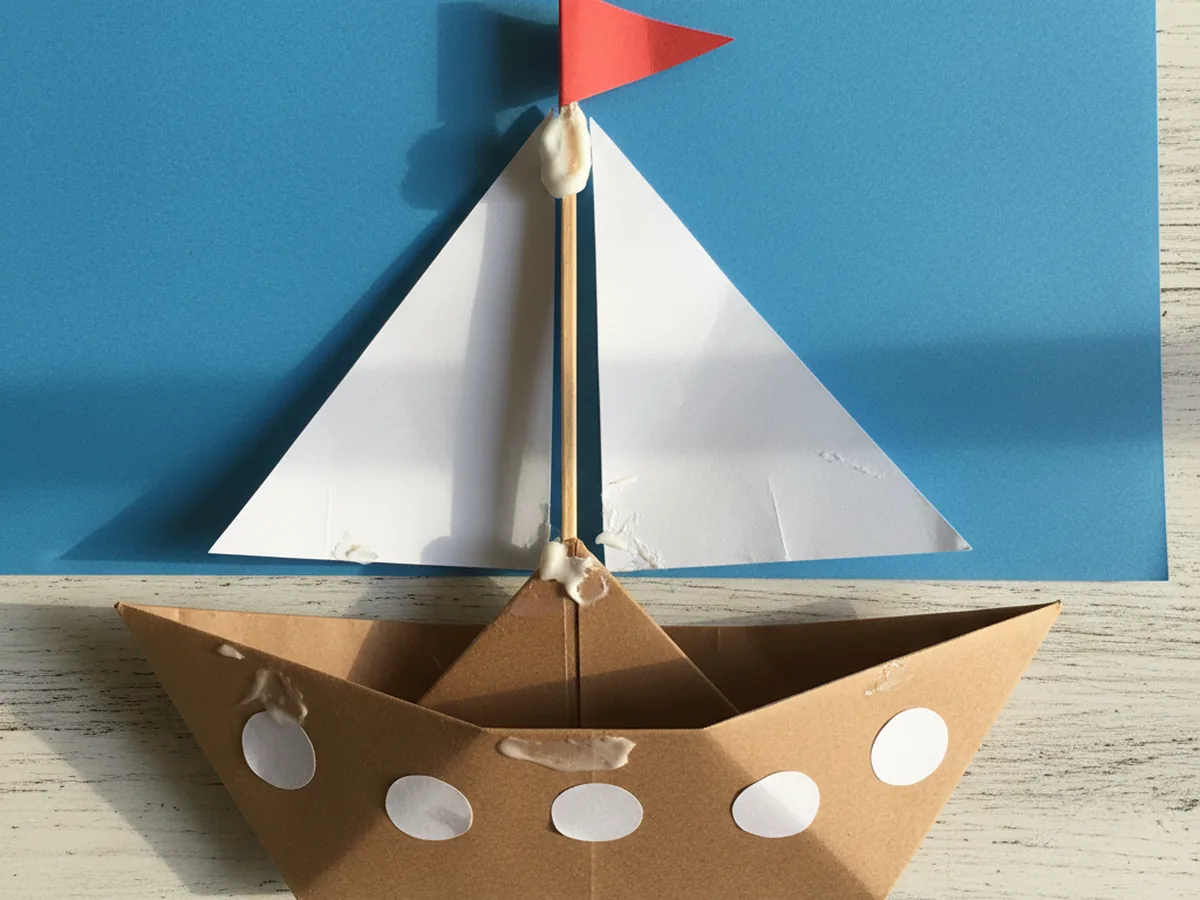 Paper ship with a small red triangle flag glued to the top of the mast and three white circle portholes along the side of the brown hull