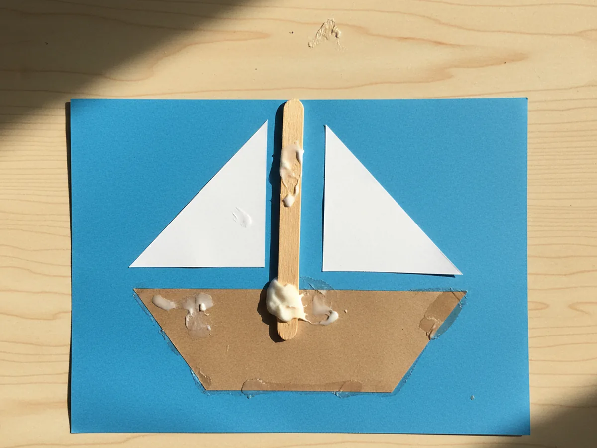 Wooden craft stick mast with white sails glued upright onto the brown paper hull, balanced in the center of the ship