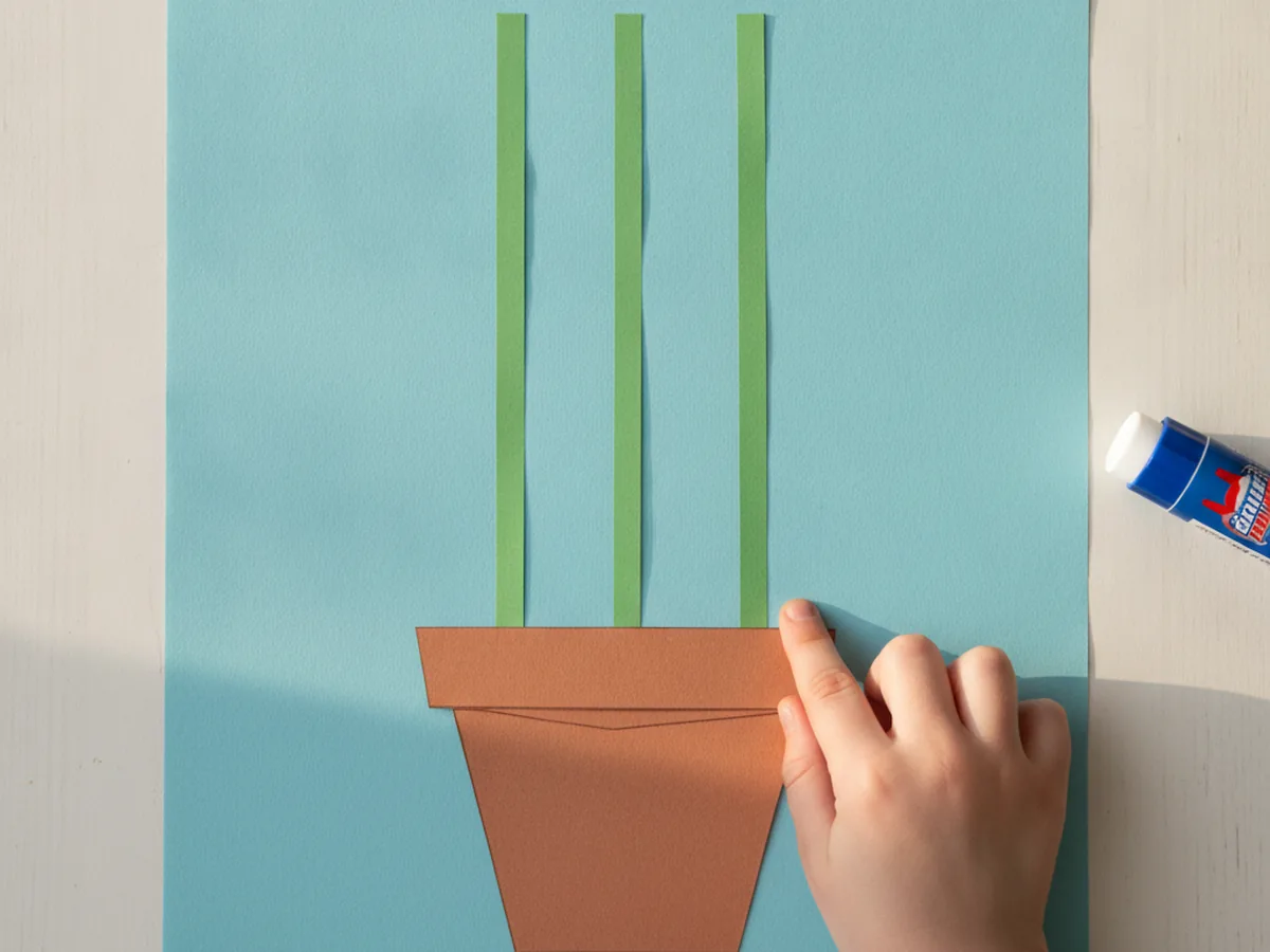 A brown paper pot and three green stems glued onto a light blue paper background for a paper tulip craft