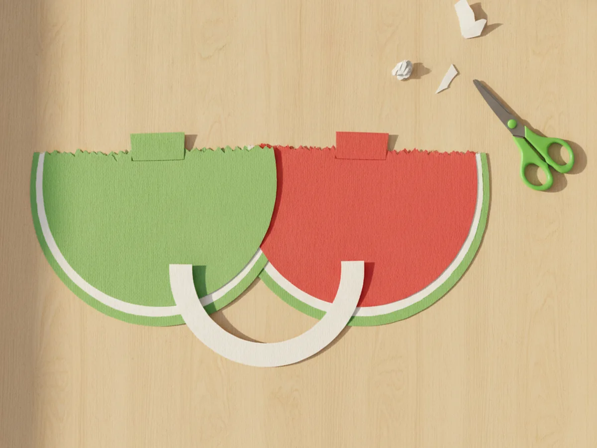 A thin white crescent paper strip cut to fit between the green rind and red fruit of a paper watermelon craft