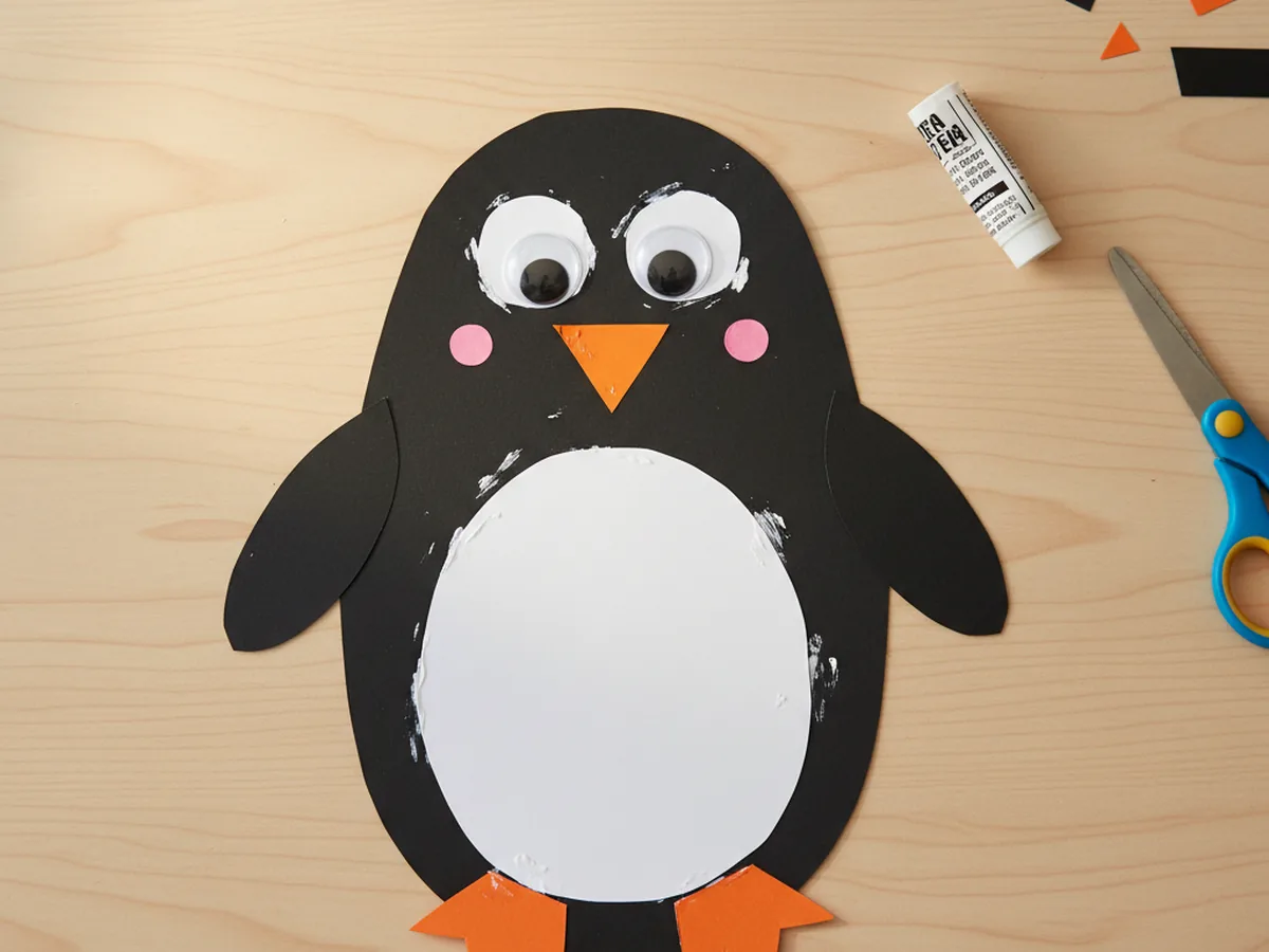 The penguin paper craft now has two narrow black oval flippers glued to the sides of the body and two small orange feet glued at the bottom