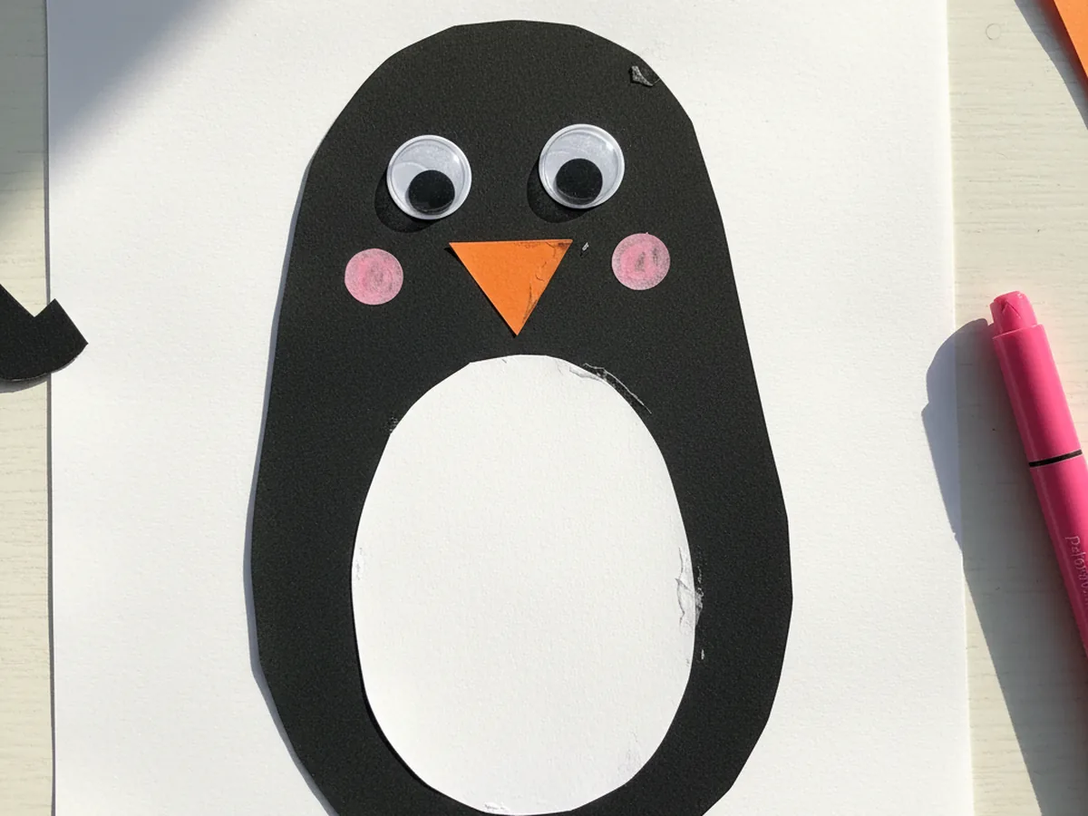 The penguin face decorated with two googly eyes above the orange beak and two soft pink cheek dots drawn with marker