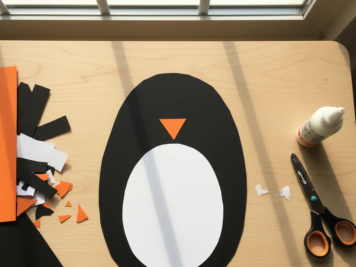 A small orange paper triangle glued just above the white belly on the black penguin body to form the beak