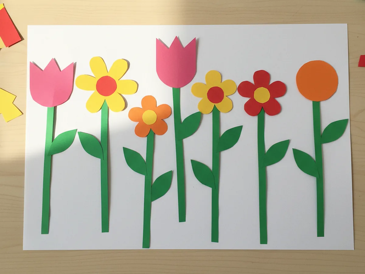 A handmade construction paper flower garden with bright tulip and daisy shapes on green stems