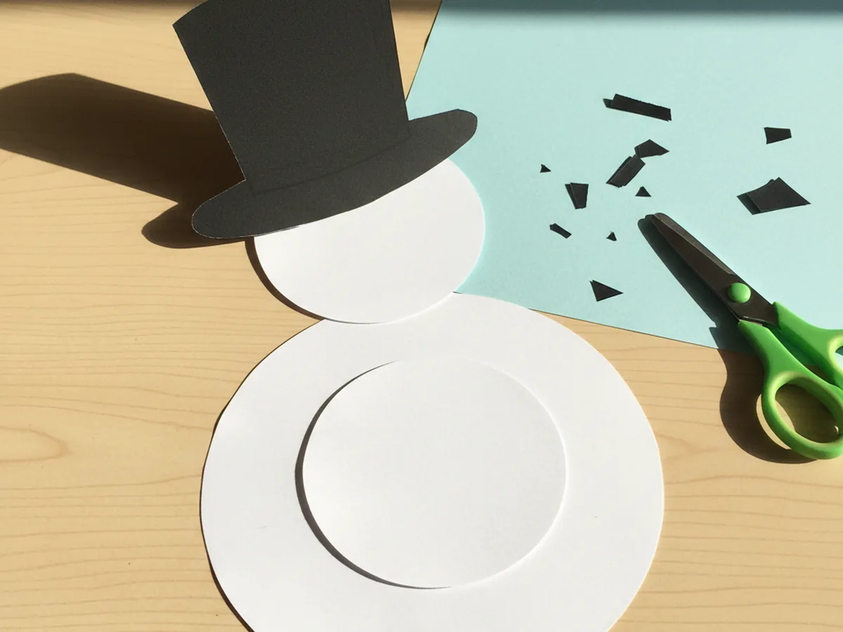 Snowman paper craft with a black construction paper top hat glued to the head circle on the blue background