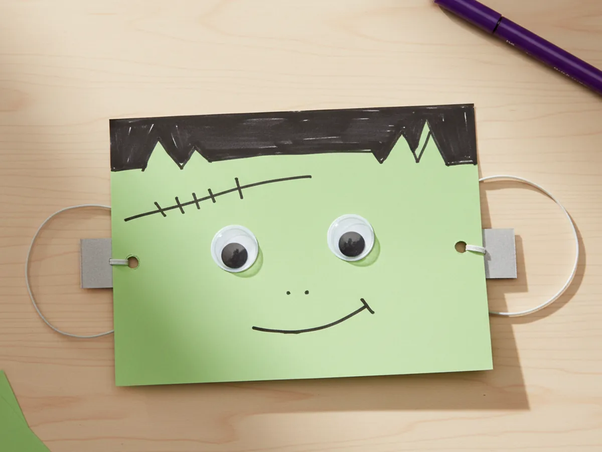 Handmade green paper Frankenstein mask with black hair, neck bolts, googly eyes, and marker stitches