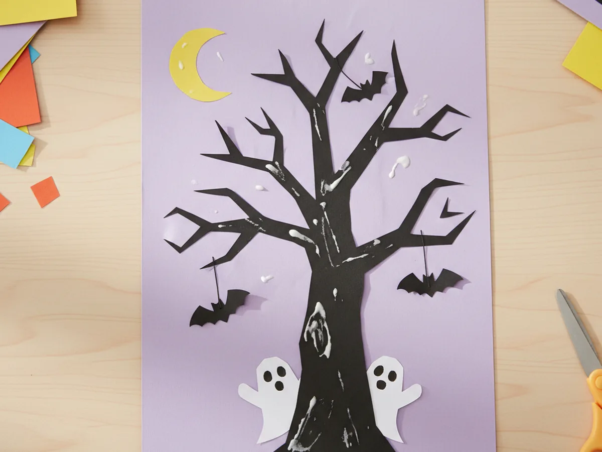 Handmade paper spooky tree scene with a black bare tree, paper moon, and small bats on a purple background