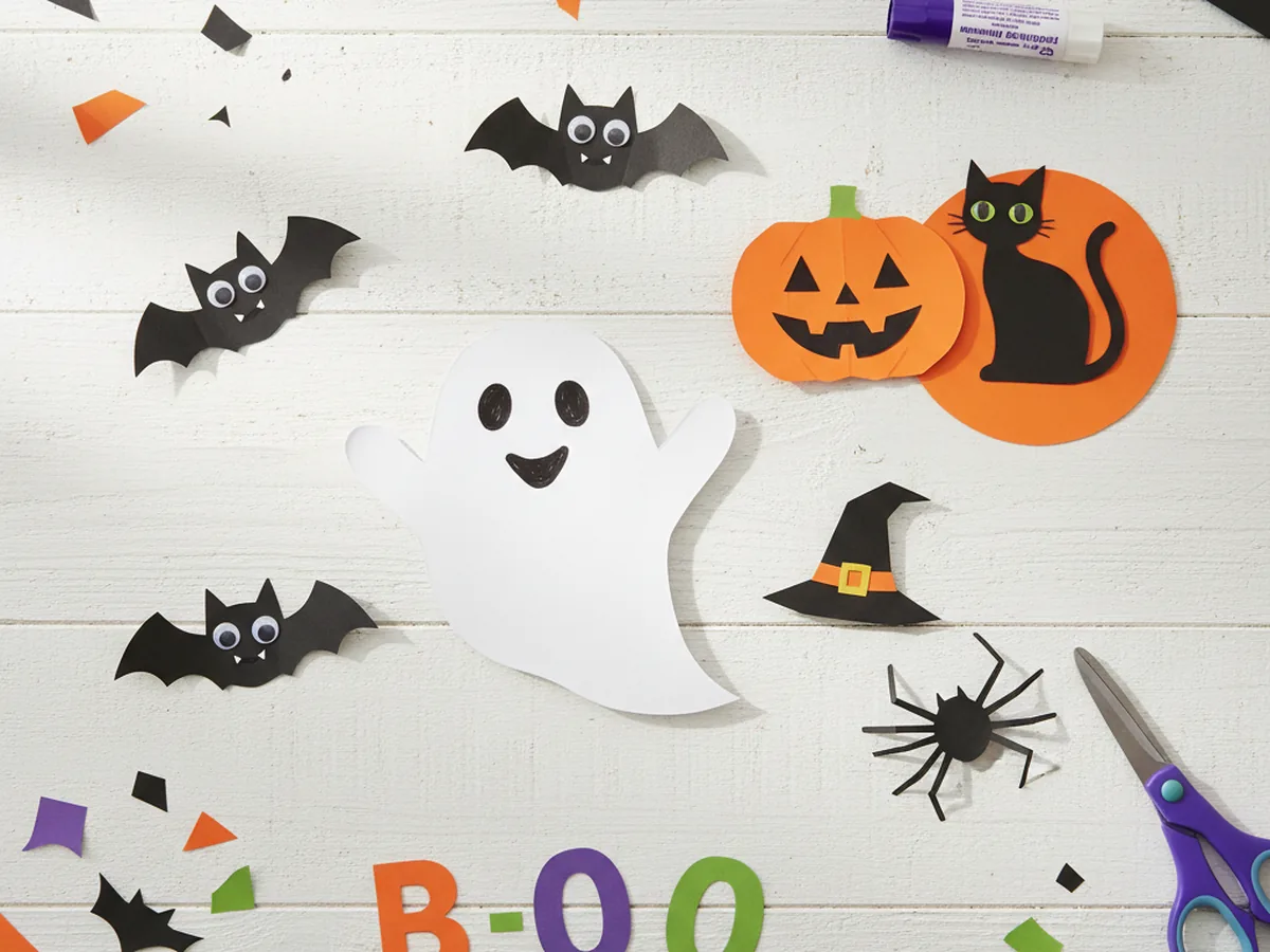 A colorful spread of handmade spooky paper crafts including ghosts, bats, pumpkins and spiders on a craft table