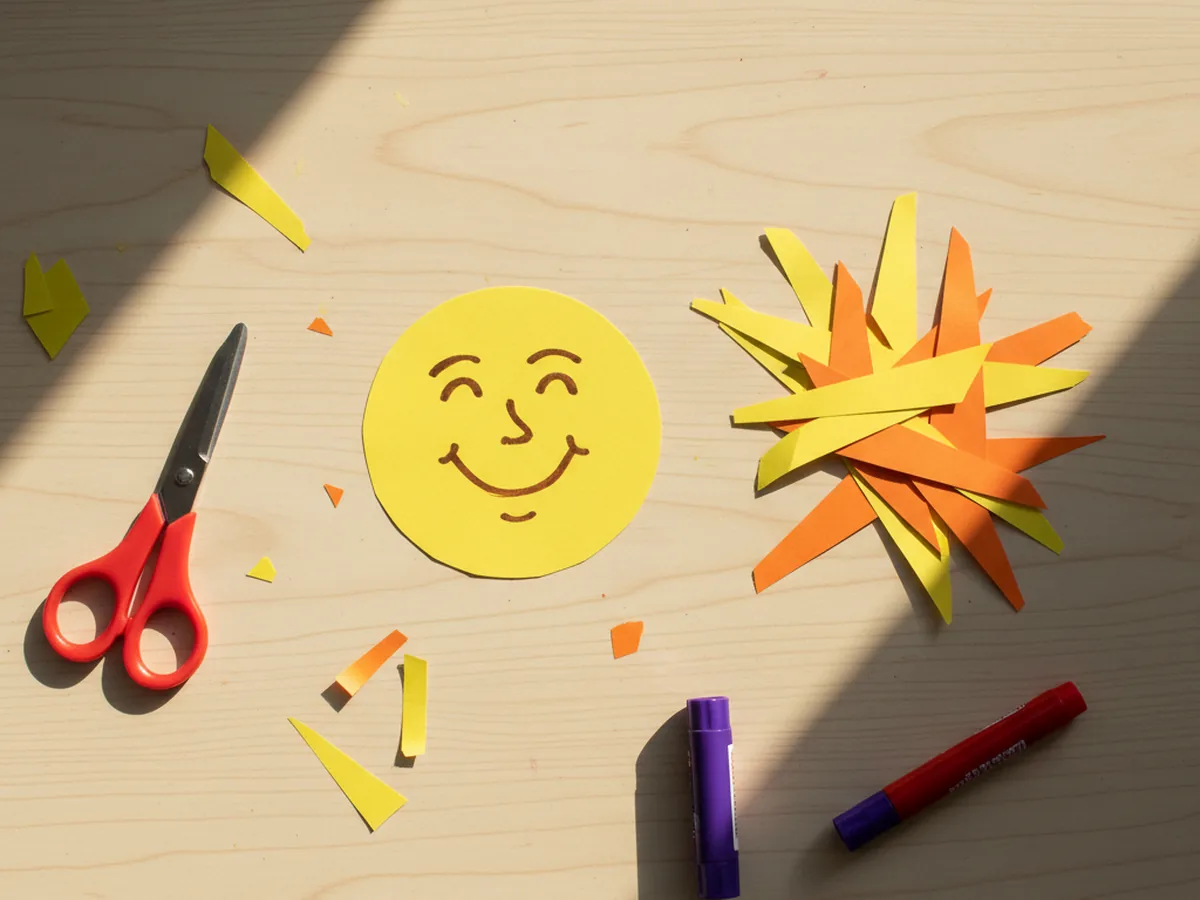 Yellow and orange triangular paper sun rays freshly cut and arranged in a small pile next to the yellow circle on a craft table