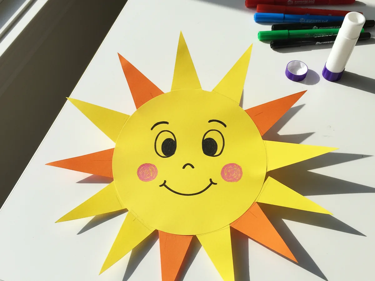 Bright yellow and orange sun paper craft with a smiling face displayed on a white craft table