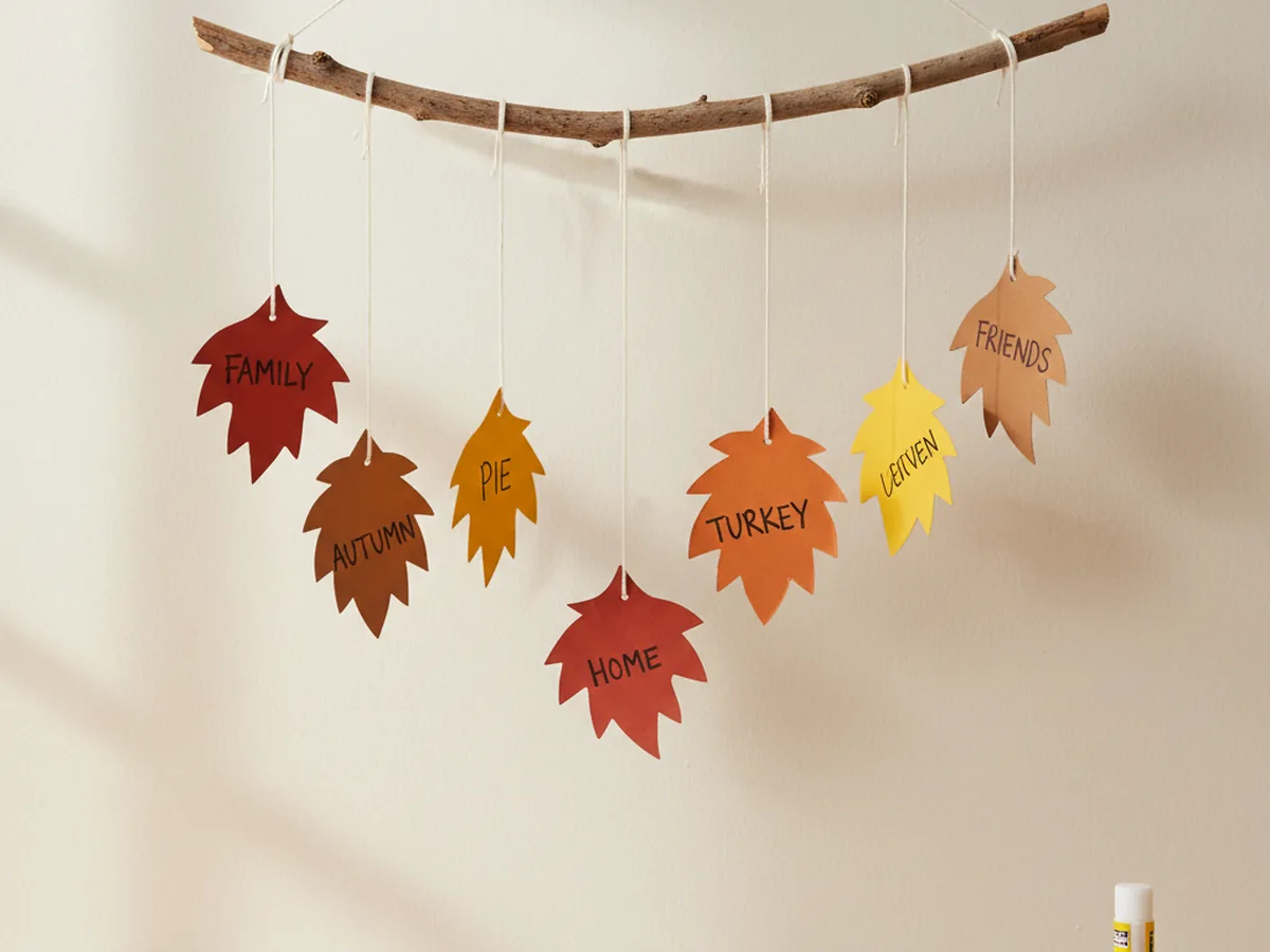 A handmade thankful leaf mobile with colorful fall paper leaves hanging at different heights from a small wooden stick