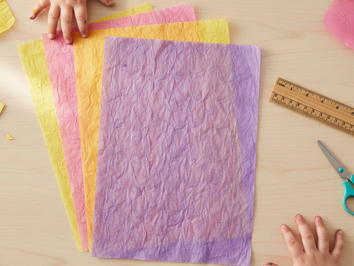 Colorful tissue paper sheets in pink, yellow, and purple stacked neatly on a craft table